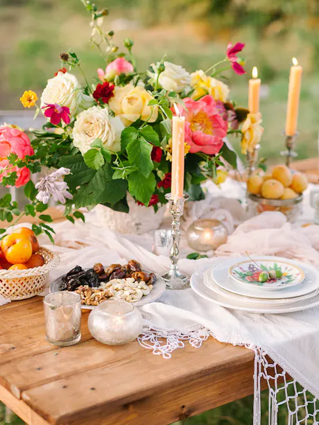 Outdoor summer dining table with garden flower centerpiece, candlelight, fresh fruit, and seasonal appetizers