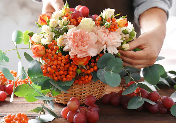 A local floral designer heaps pink, orange and red flowers and berries into a large gift basket