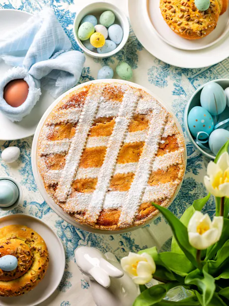 Easter pie at the center of a spring-themed table decorated with pastel-painted eggs, white tulips, candy eggs, and pastries