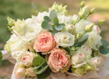 Lush bouquet of pink and white roses with green foliage, arranged tightly together; set against a softly blurred outdoor background with natural sunlight.