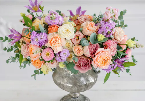 Spring Holiday Arrangement of pastel roses, carnations, and lavender blooms in a silver vase.
