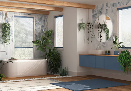 A contemporary bathroom featuring a bathtub and a floating sink under a round mirror, surrounded by hanging plants, wooden beams, and large windows with natural light streaming in.