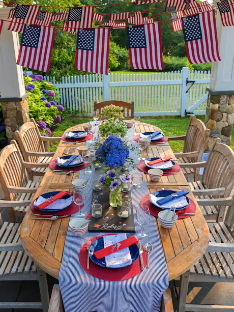 Outdoor Fourth of July table setting with flags, blue hydrangea centerpiece, and red white blue dinnerware