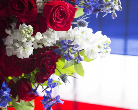 Bouquet with red roses, white hydrangea, and blue flowers against an American flag background