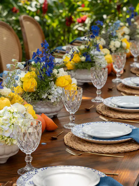 Outdoor spring tablescape with yellow, blue, and white floral centerpieces on a dining table
