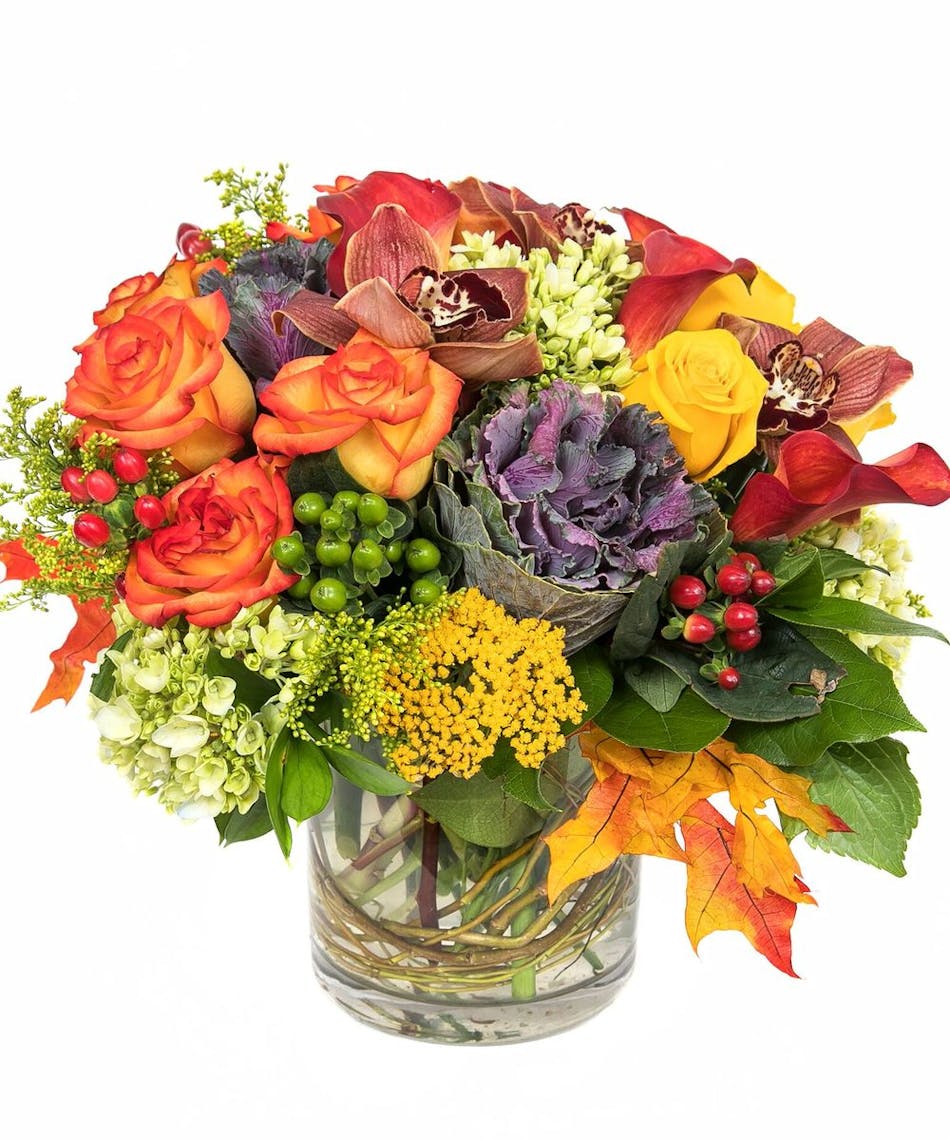 Features roses in red and orange along with red and green hypericum and green hydrangeas â skillfully designed in a cylinder vase with curly willow tips and leaves.