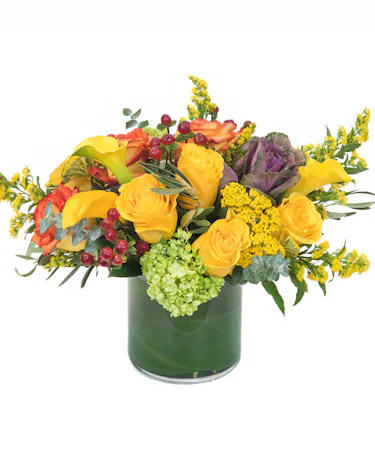 Features roses in red and orange along with red and green hypericum and green hydrangeas – skillfully designed in a cylinder vase with curly willow tips and leaves.